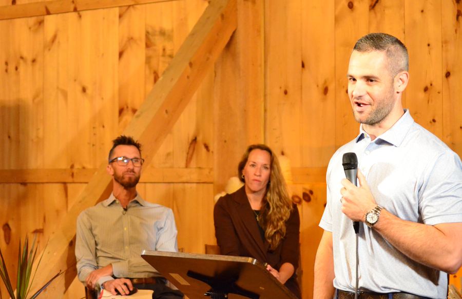 Blake Schindler speaking, with the other speakers seated behind him